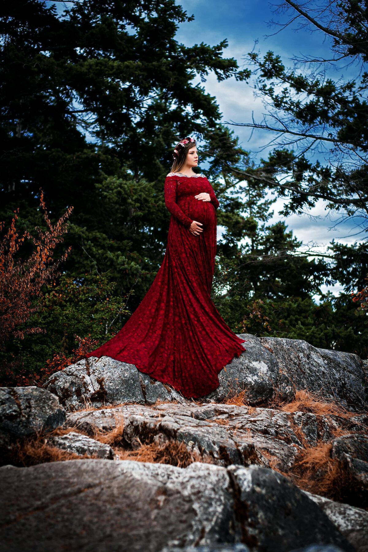 Expectant mom-to-be in red lace dress on a rocky mountain top.