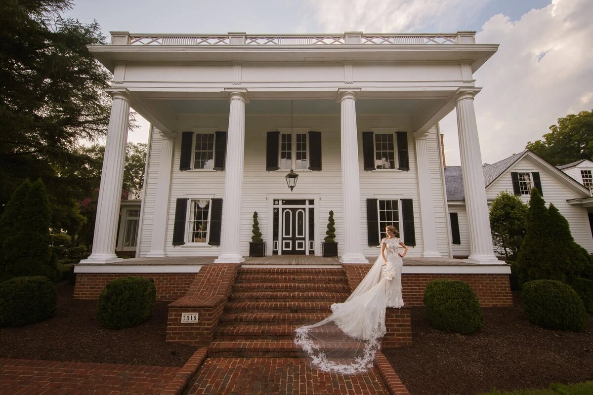A bride standing on the brick pillar in front of a large house