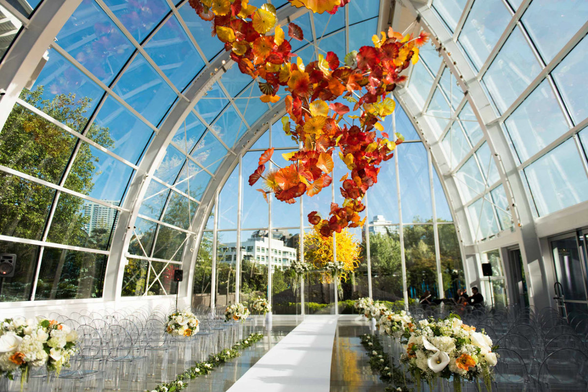 Perfect sunny day for a wedding in the glass house at Chihuly with wedding aisle of large white and orange wedding flowers