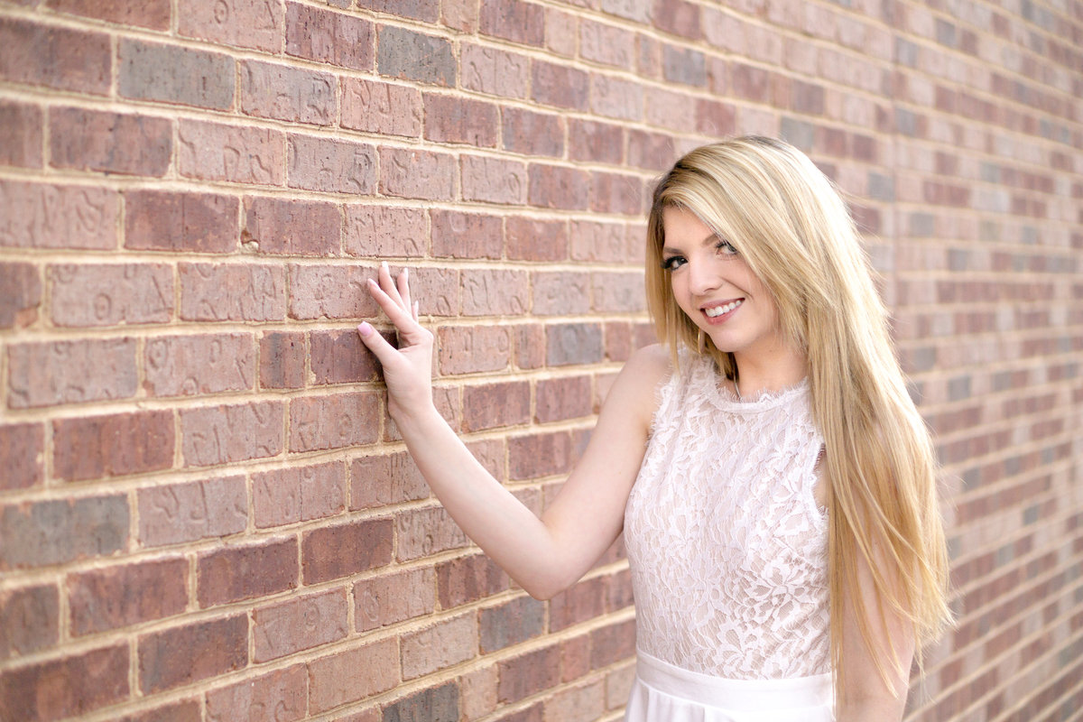 Girl in white dress with long beautiful blonde hair stands next to a brick wall