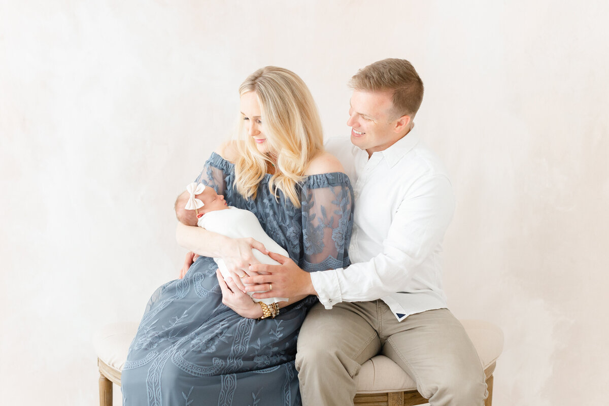 A Northern Virginia Newborn Photography photo of two parents sitting on a bench looking down at their newborn baby in their arms