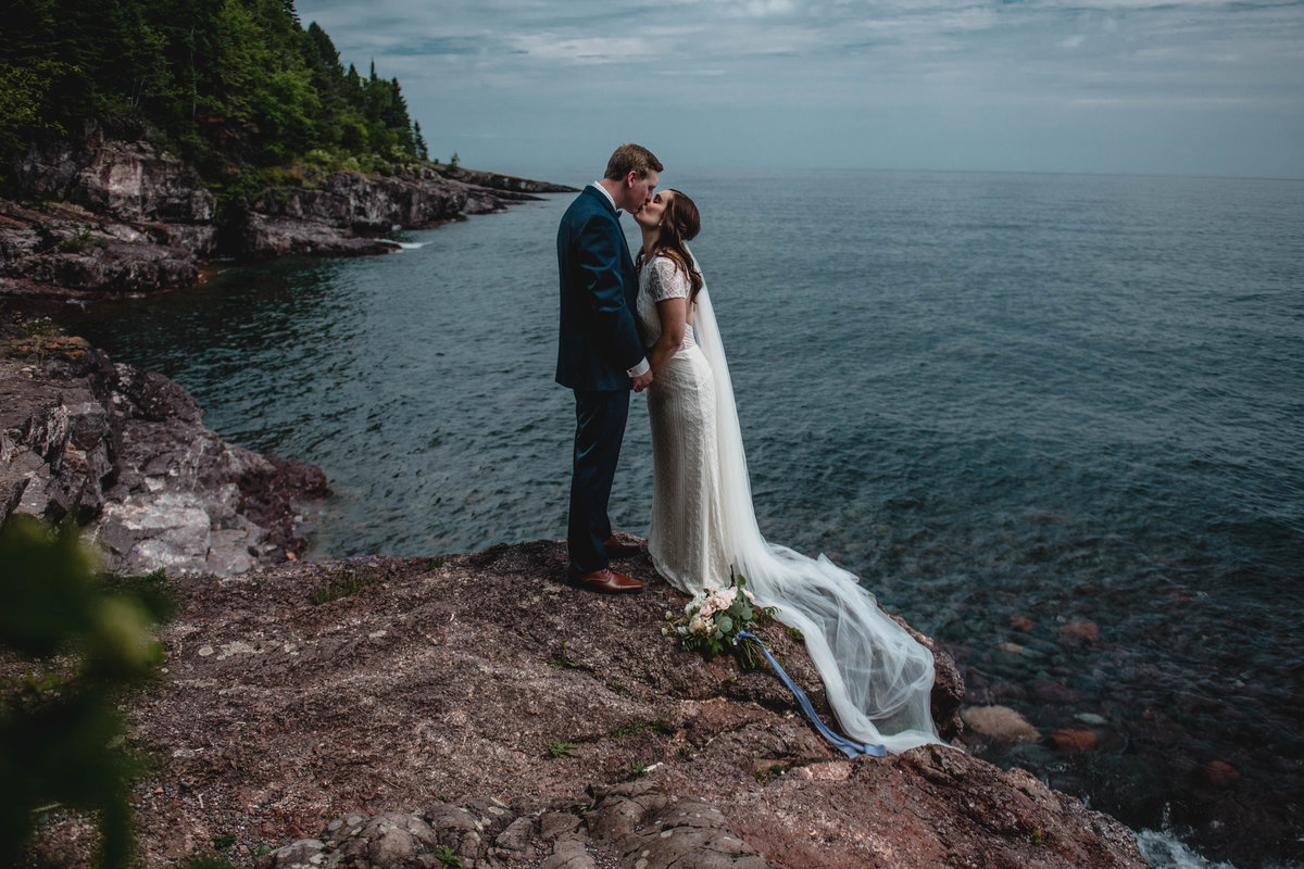 Bride and groom kiss on rock overlooking Lake Superior.