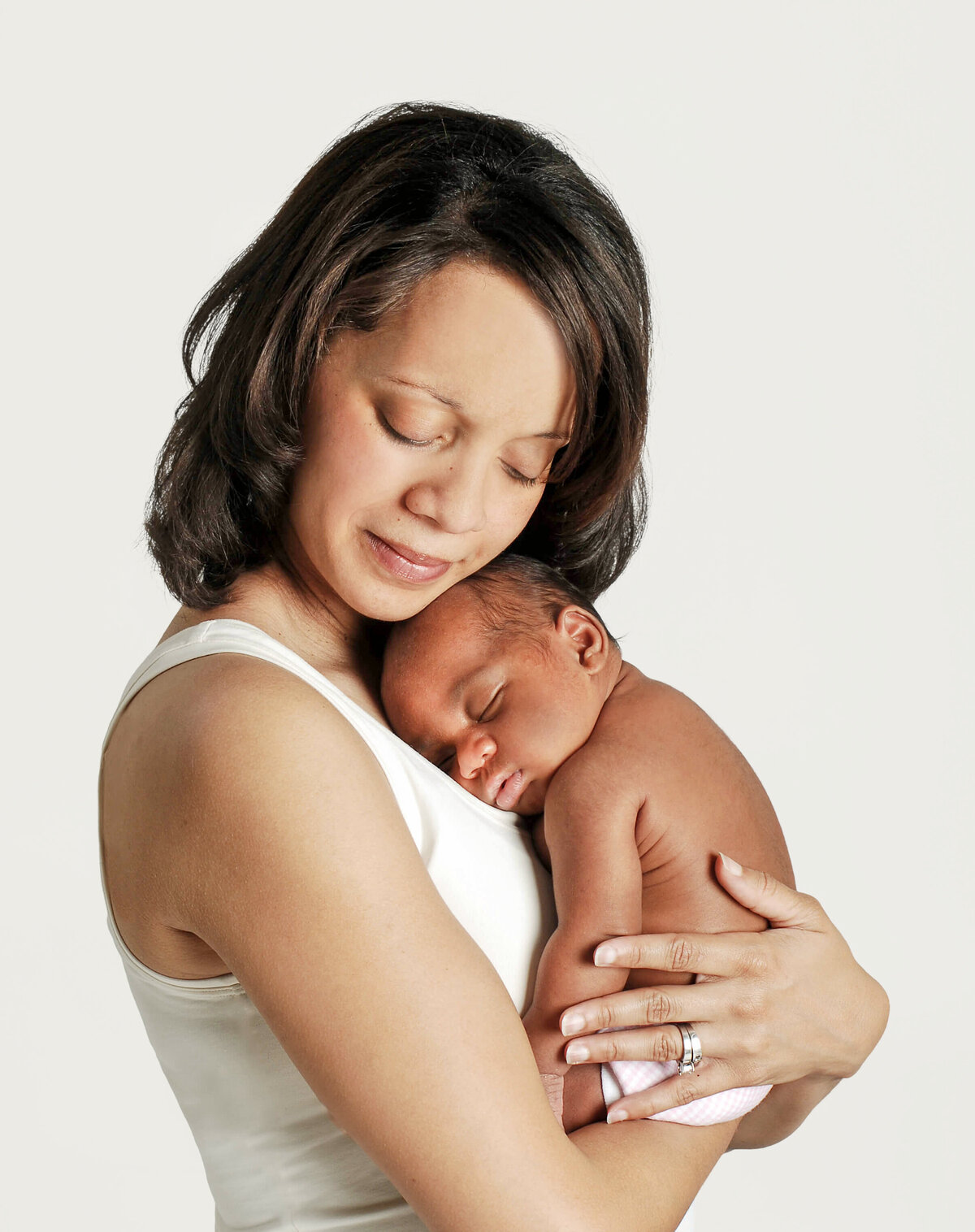 A new mom in a white tank top holding her diaper wearing baby close to her chest, and resting her cheek on his head.