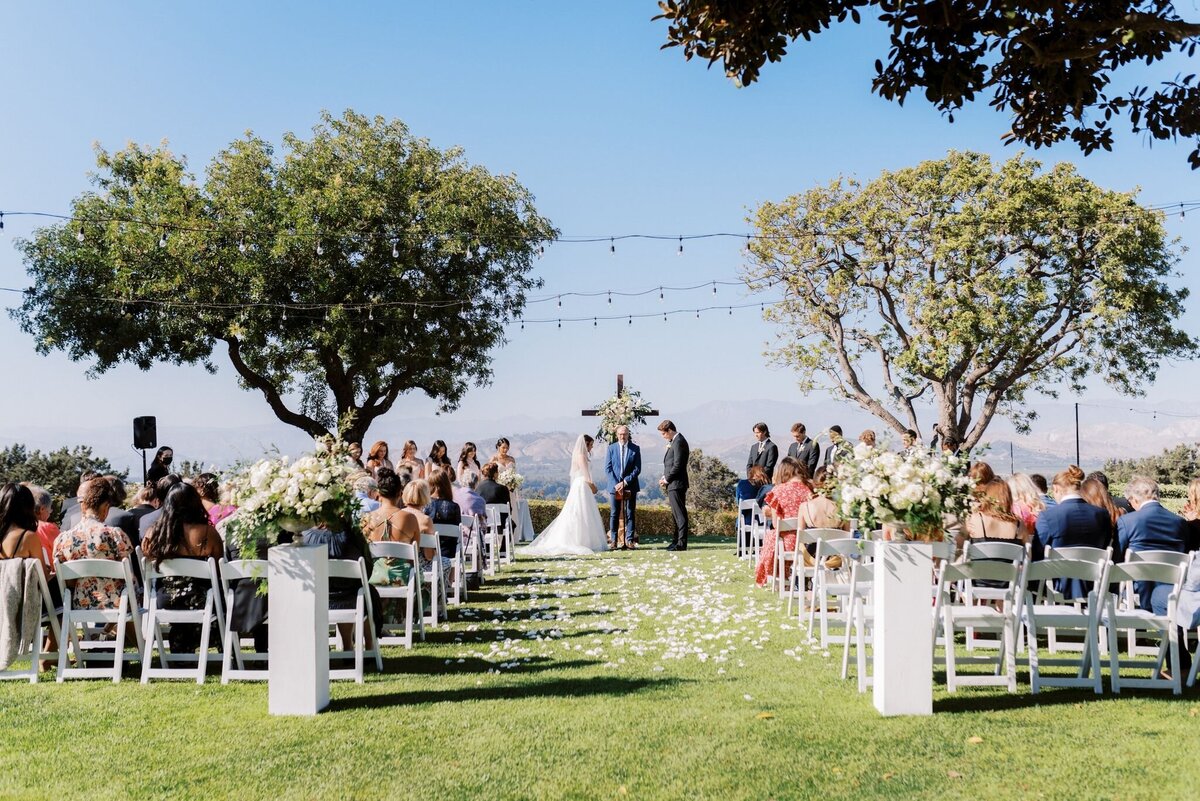 The wedding ceremony with the wedding arbor cross full of white flowers.