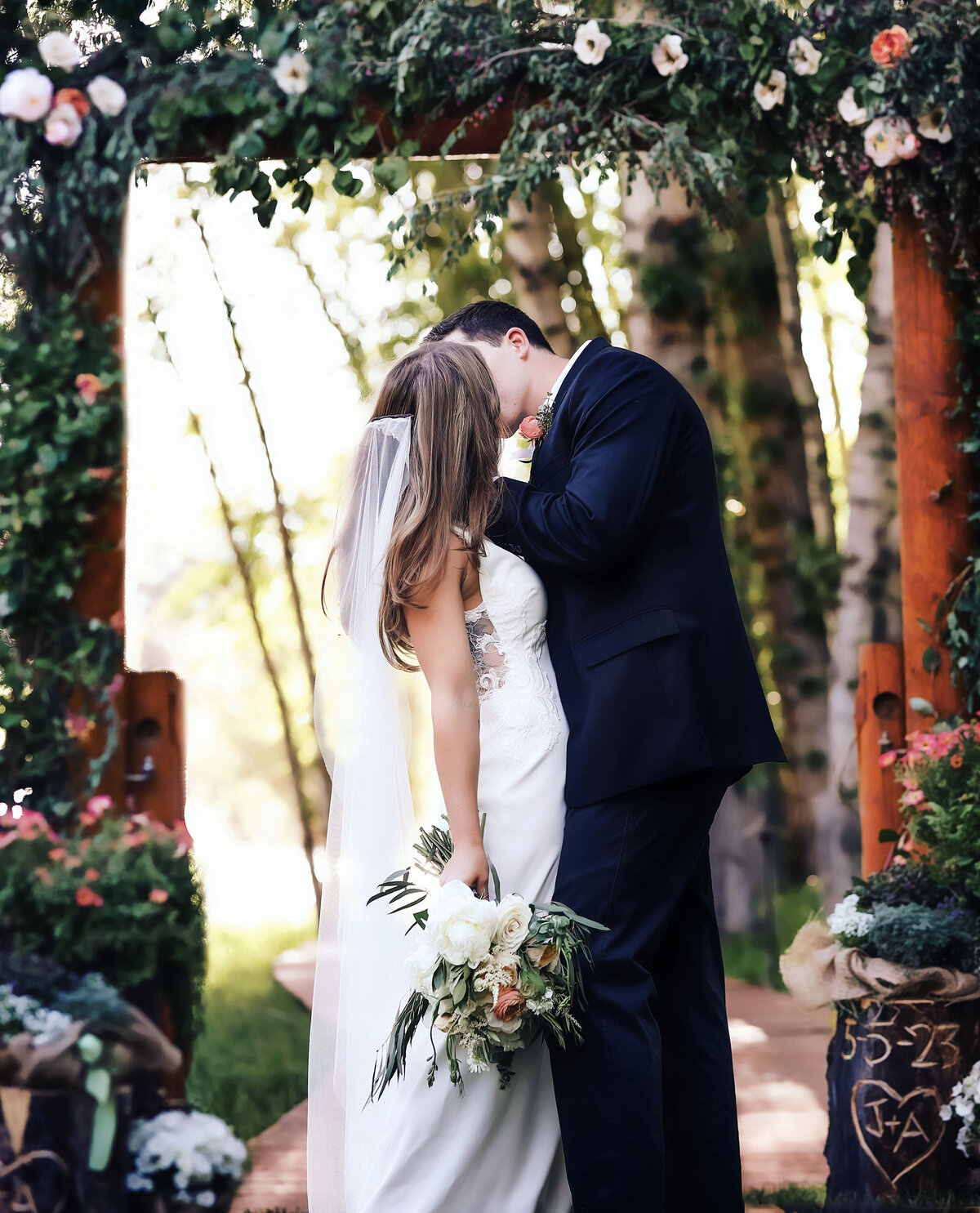 The moment the bride and groom kiss, underneath a beautiful and colorful flowered alter in their aspen wedding.