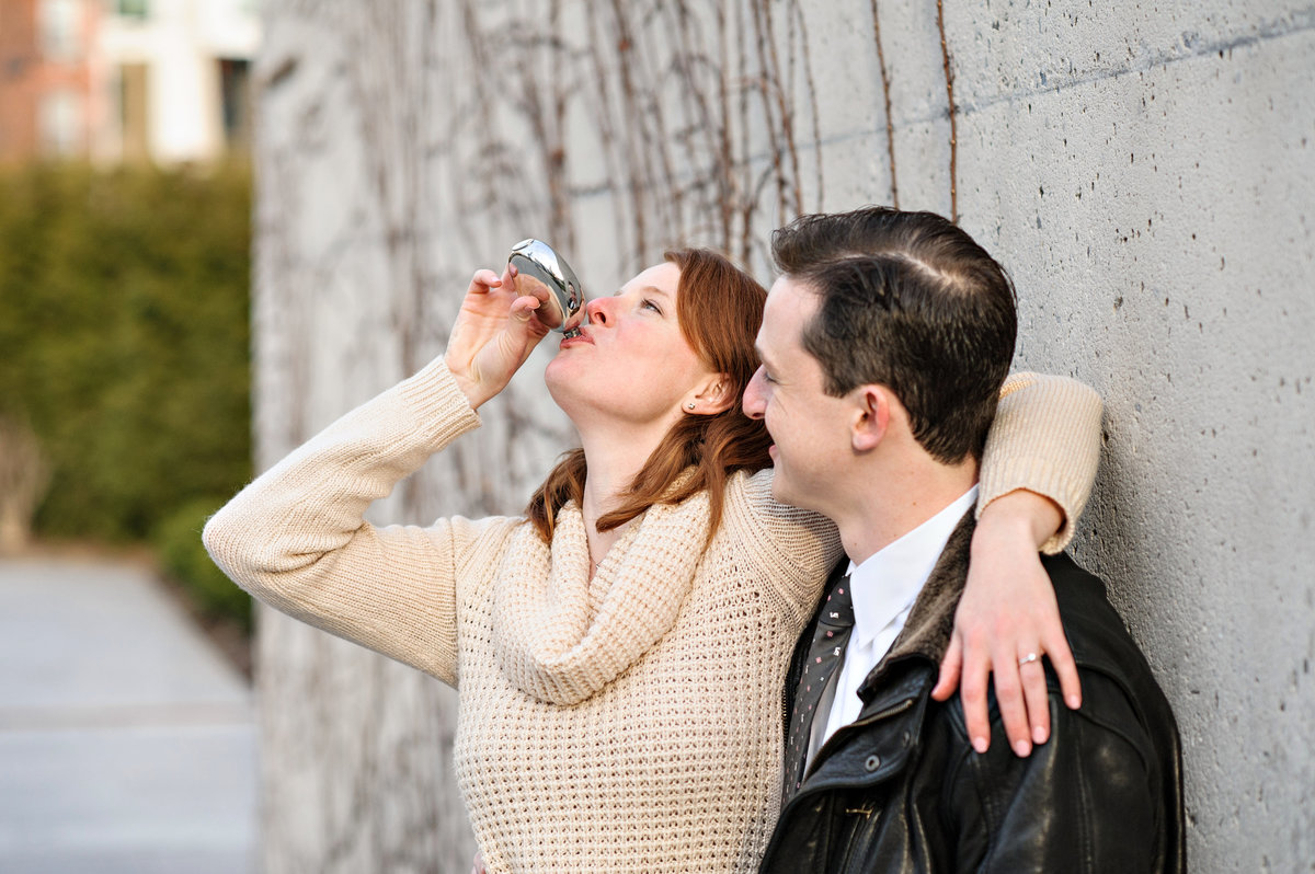 A engaged couple sip whiskey to warm them up during their fall engagement session.