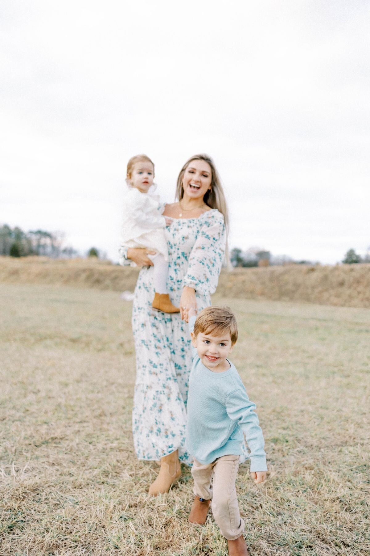 Son pulls mothers hand running while woman holds baby.