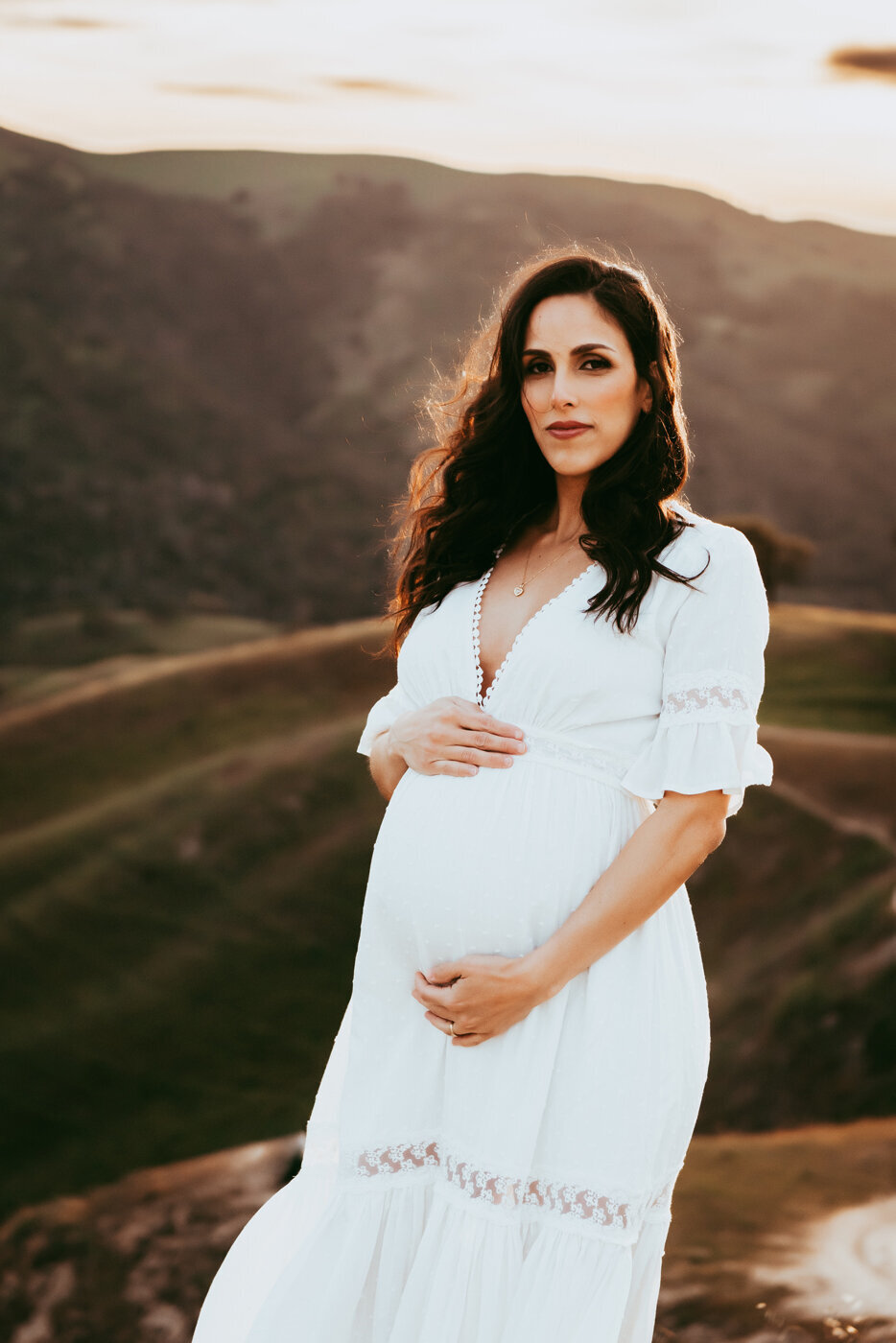 Stunning pregnant mama looking at the camera wearing a white dress