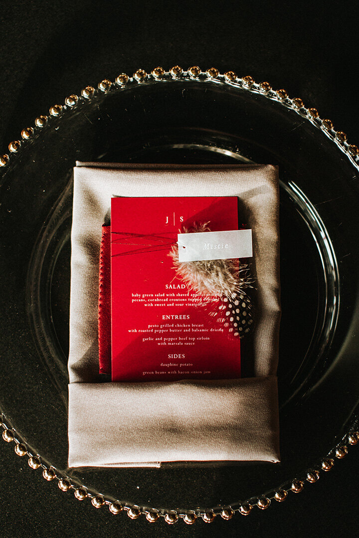 Red dinner menu with white font set atop a napkin and clear plate with gold details.