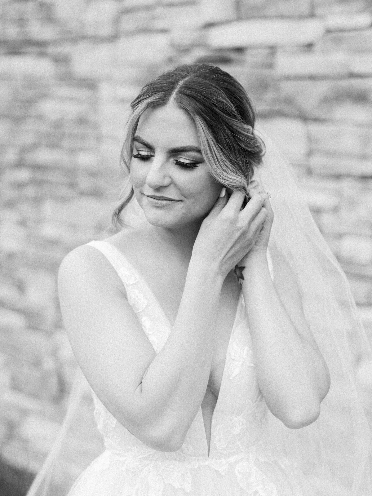 A black and white image of a bride putting in her earrings on her wedding day