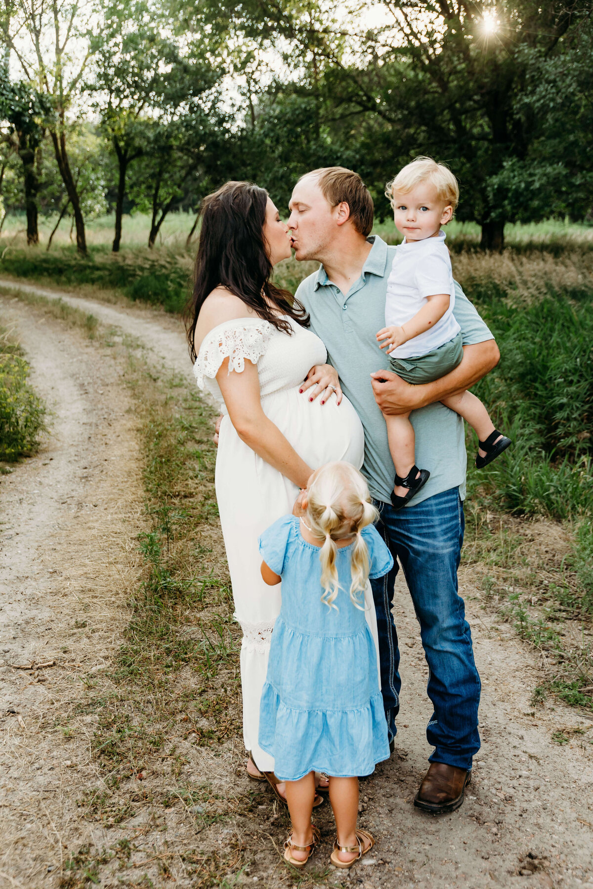 Mom and dad kiss while the kids make adorable faces on the dirt road.