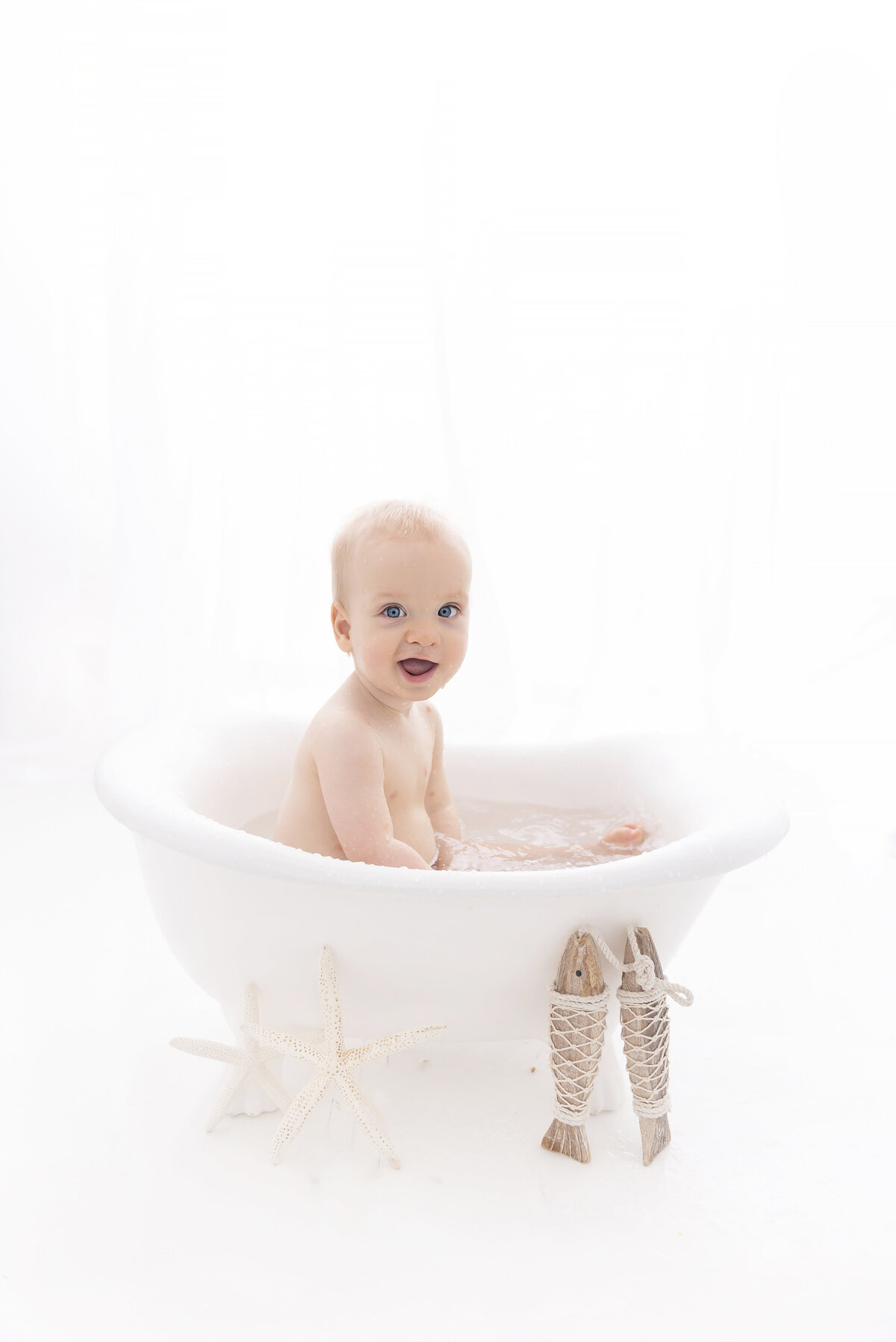 A toddler boy plays in a bathtub with a smile in a studio