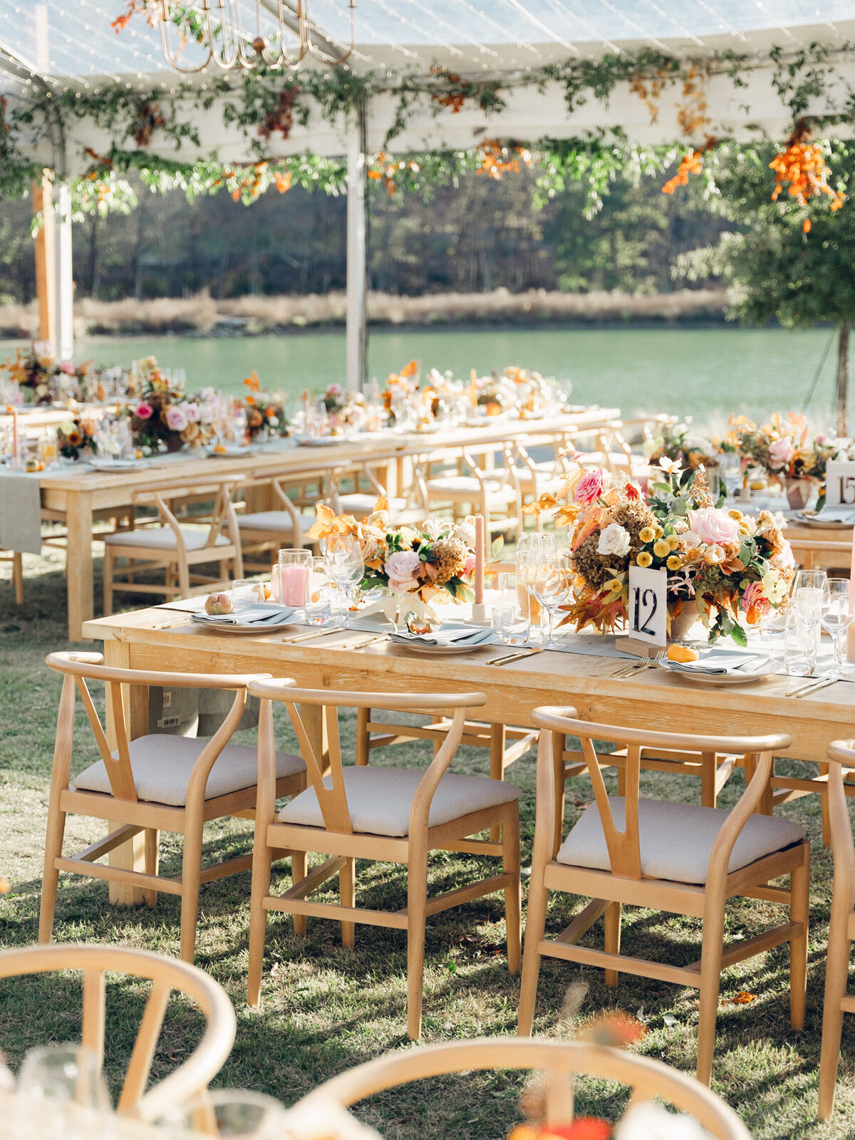 Full tablescapes of fall flowers create lush warm fall setting for wedding reception in Tennessee countryside. Wedding colors in blush, tangerine, mustard yellow, caramel, and honey. Wedding fall florals consisting of roses, clematis, ranunculus, brown tulips, and fall foliage. A collection of low centerpieces and accent arrangements create lush floral wedding reception tables with styled fruit place settings. Unique and colorful candles for reception tables in pink, orange, yellow, and gold. Destination floral design by Rosemary & Finch Floral Design in Nashville, TN.