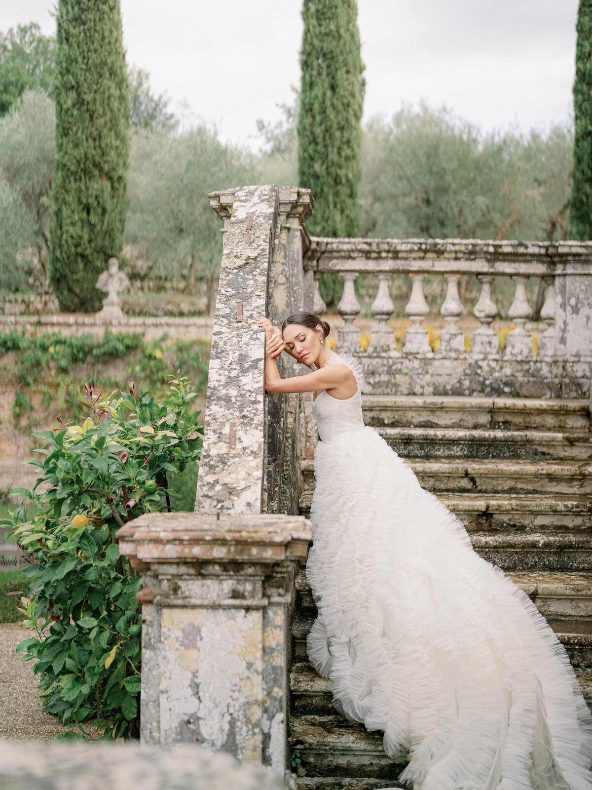 a bride in a fluffy tulle wedding dress leaning up against the stair railing at a villa in tuscany italy