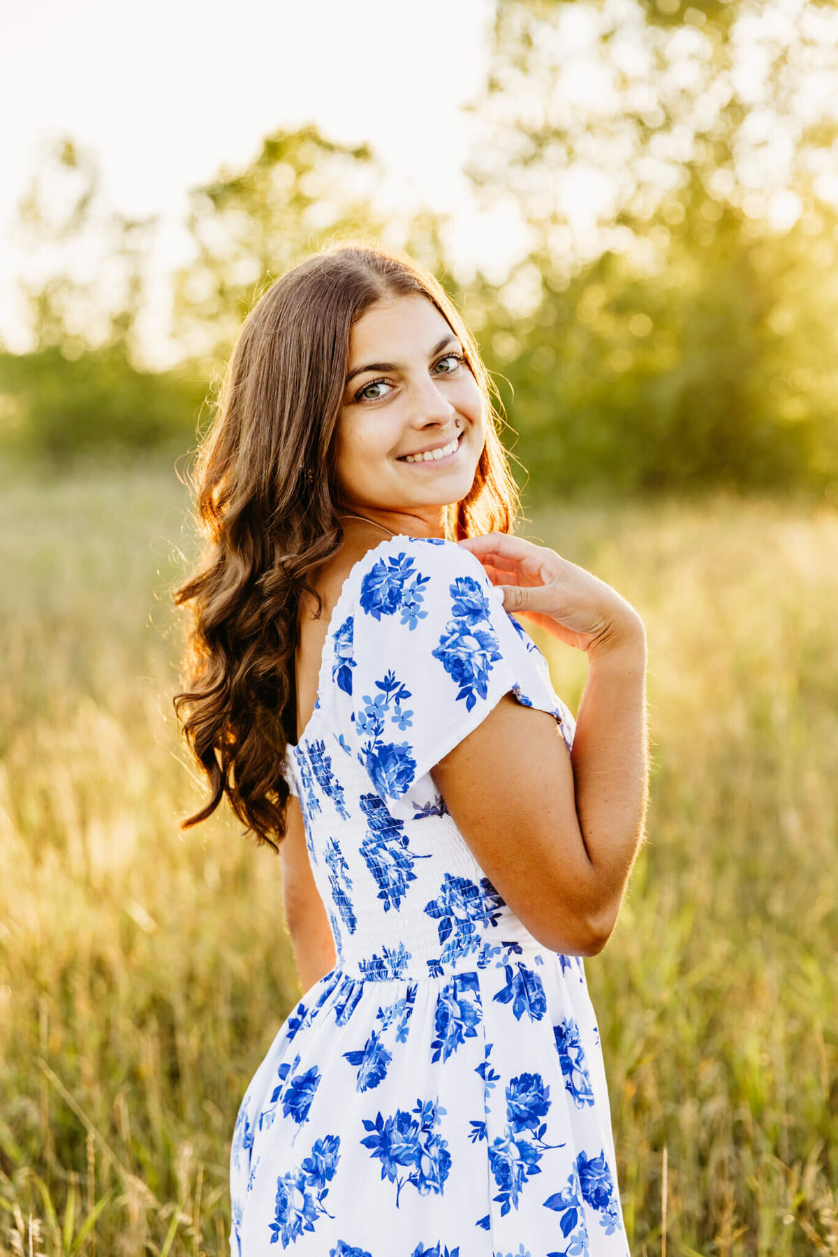 portrait of a stunning high school girl in a blue and white floral dress looking over her shoulder taken at sunset