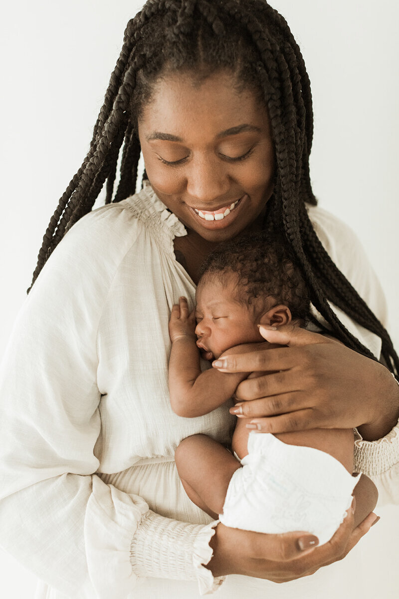 smiling mom with braids looks down at her newborn son curled up on her chest