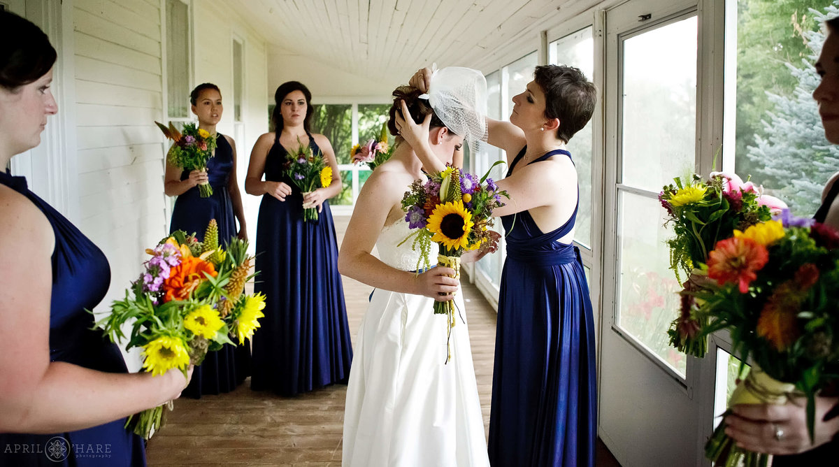 Bridesmaids wearing blue help bride with her birdcage veil on the screen in porch at Chatfield Farms in Colorado