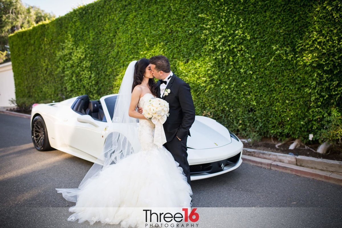 Newly married couple shares a kiss during a moment alone in front of their car
