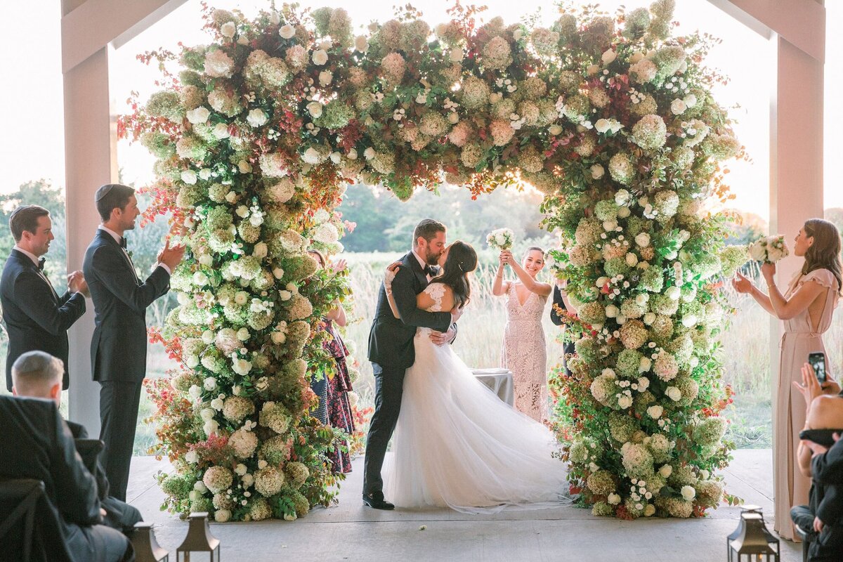 newlyweds first kiss under big floral arch
