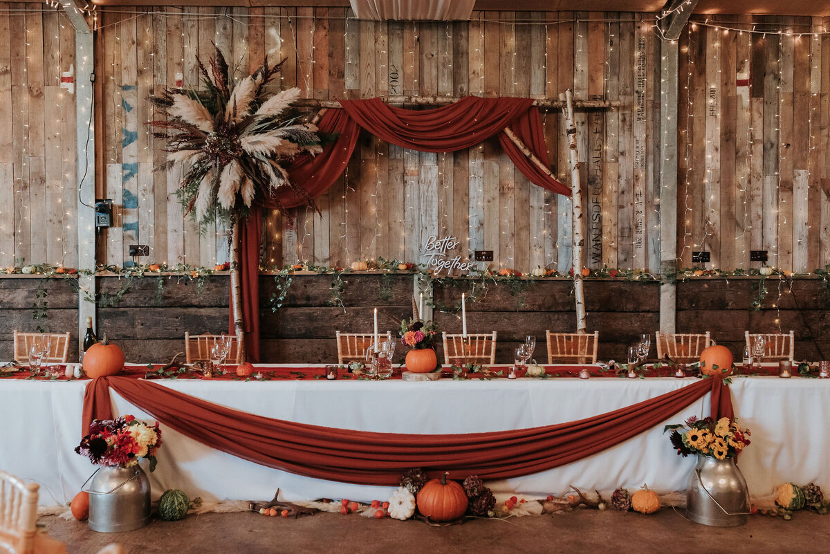 Rustic Autumn wedding table with beautiful burnt orange drapes, pumpkins and birch wood archway with pampas grass at Montague Farm, Sussex