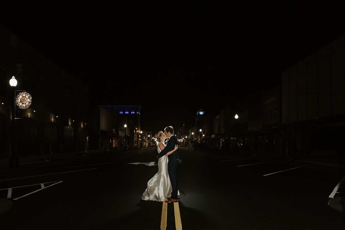 A bride and groom kiss in the street