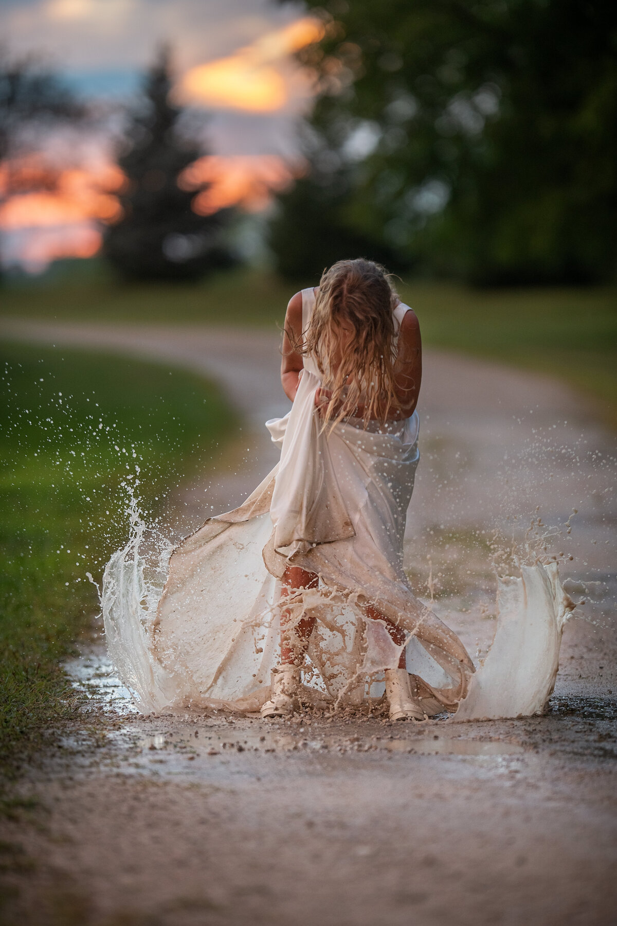 Bride jumping in muddy puddles with white wedding dress on her rainy wedding day
