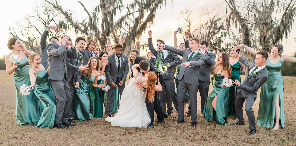 A couple kissing with their excited wedding party at sunset by JoLynn Photography, a North Carolina wedding photographer