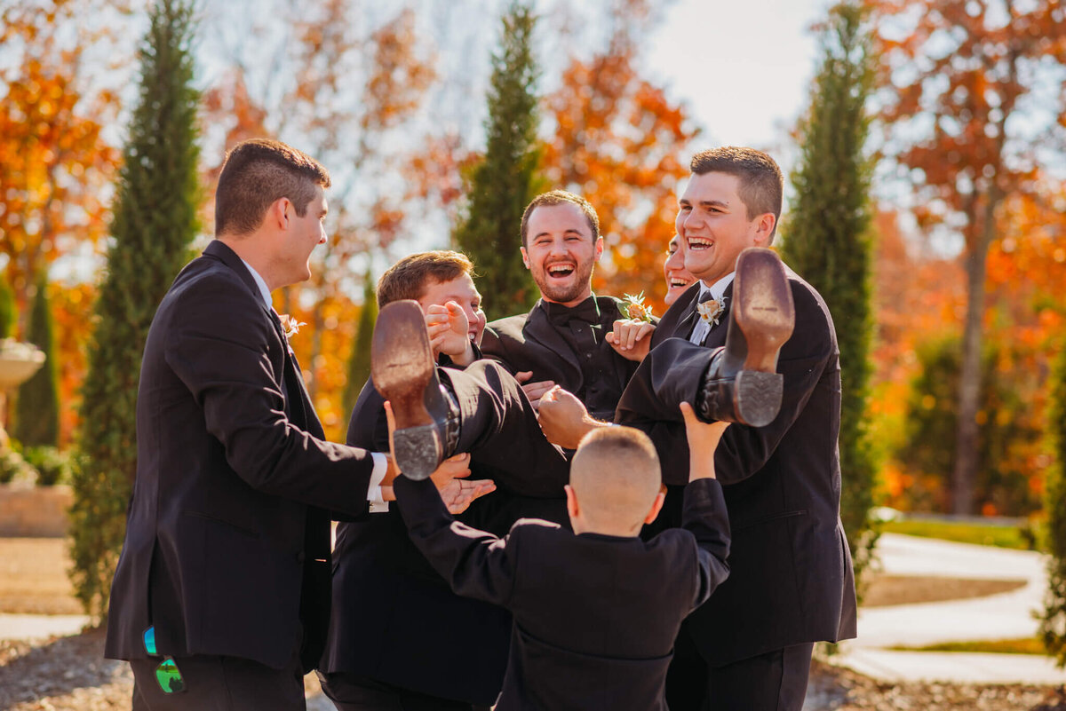 Photo of a laughing room being held in the air by his groomsmen