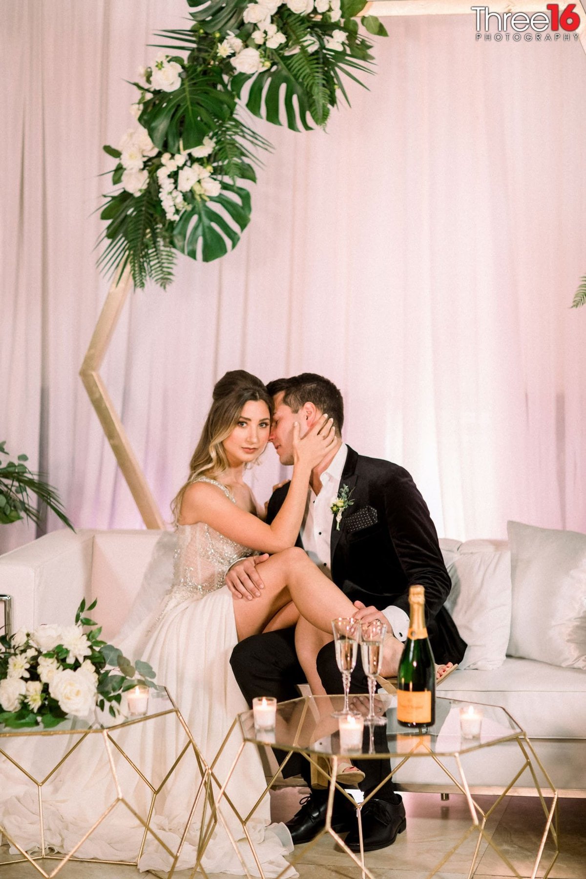 Bride places her legs across her Groom's lap and her hand on his cheek as he goes in for a kiss on her cheek