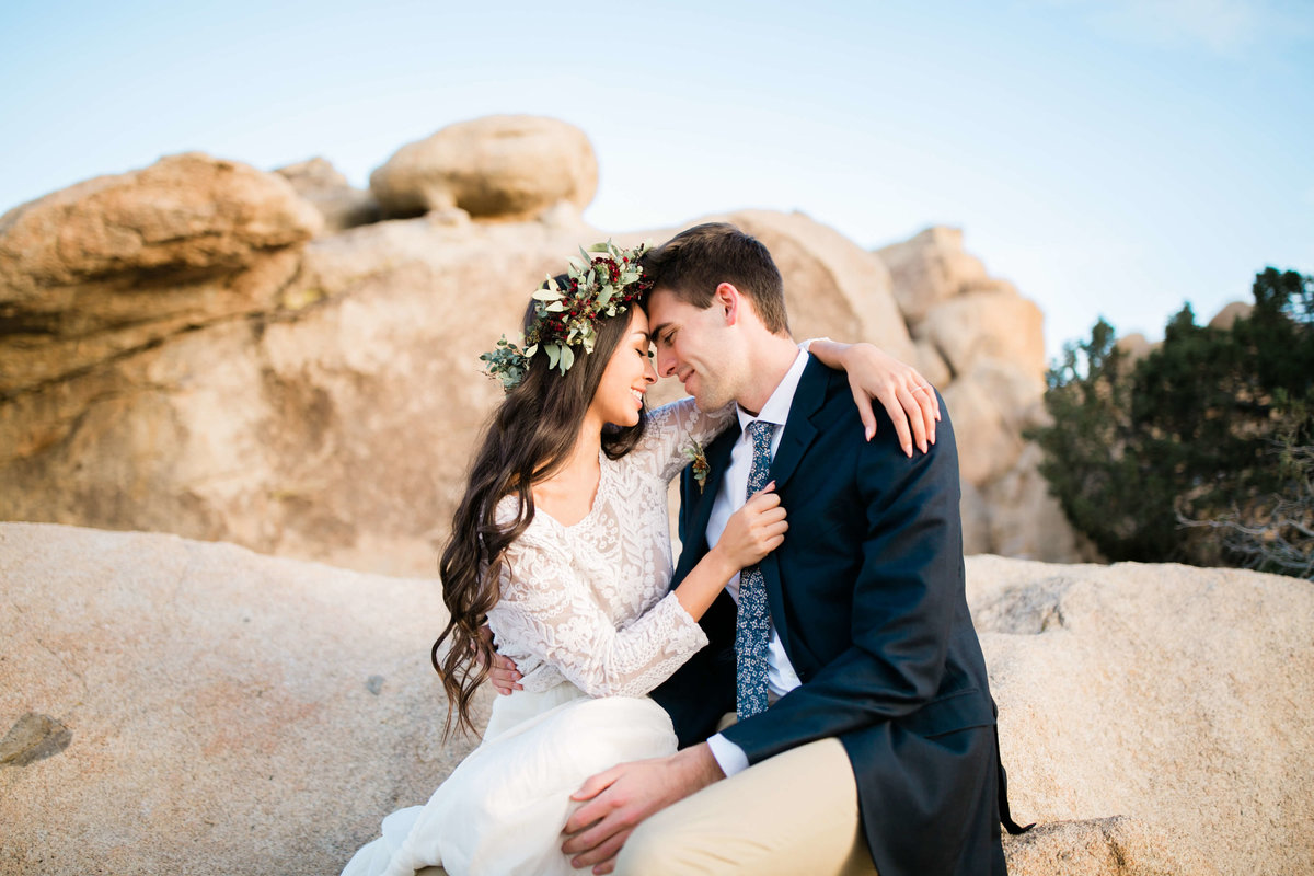 the couple snuggles in while resting on joshua trees large boulders