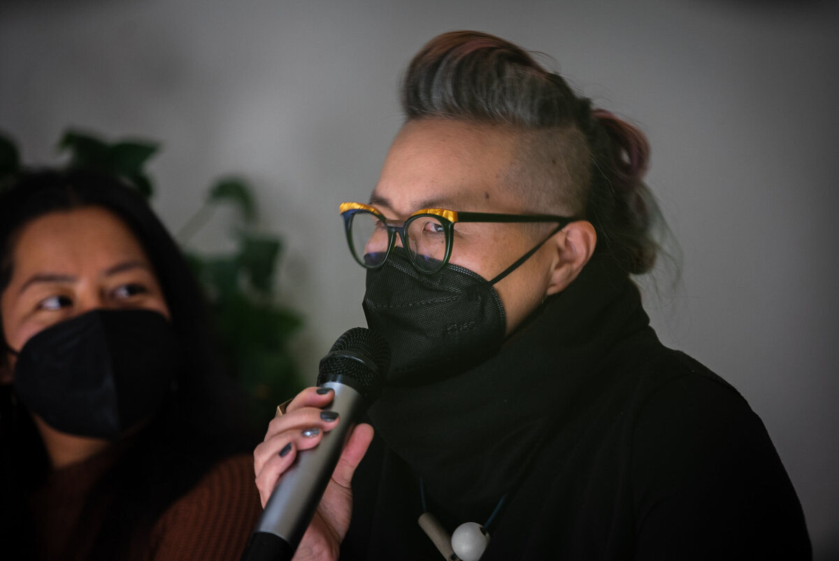 Person holding a microphone and asking a question at an event, they are wearing a mask
