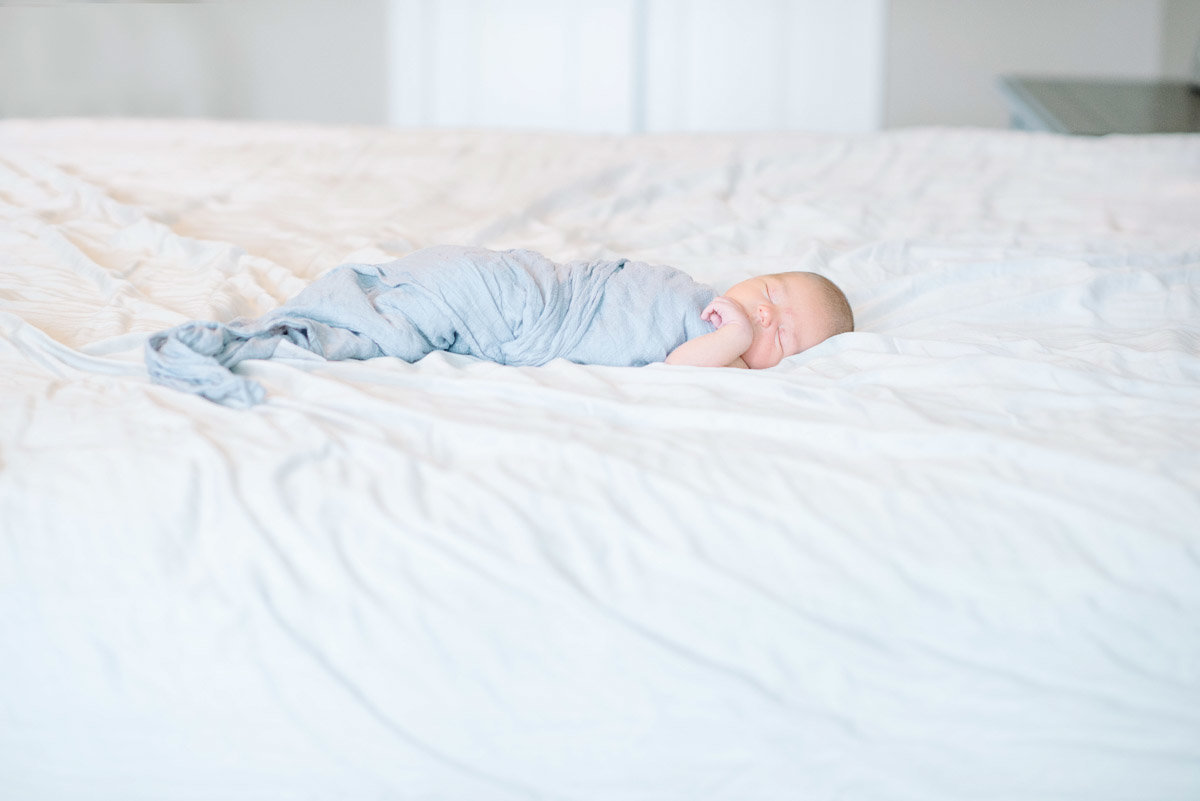 baby in light blue swaddle sleeping on white bed