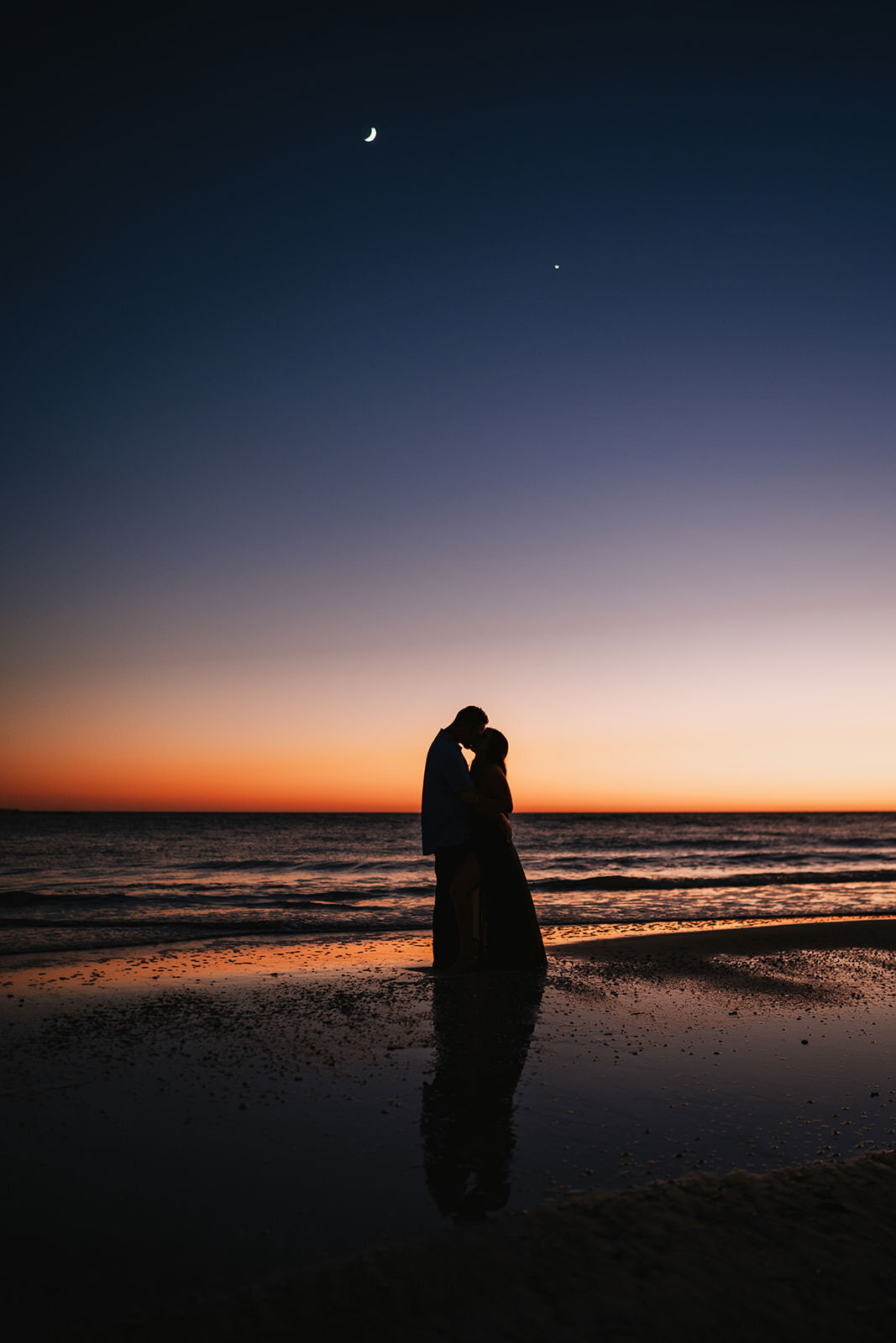 man and woman kissing on beach after sunset with the moon out