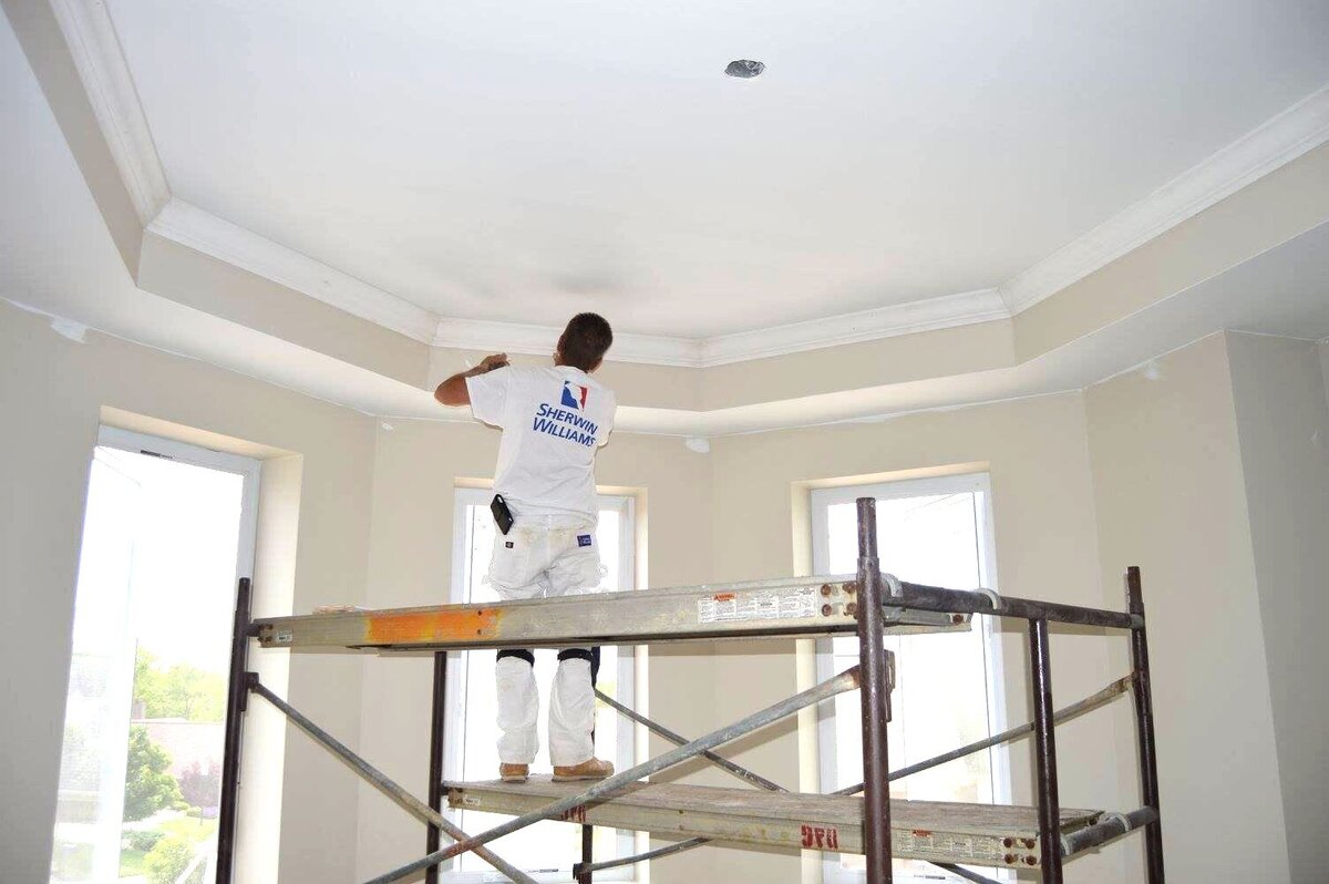 Painter stands on scaffolding to reach ceiling crown molding