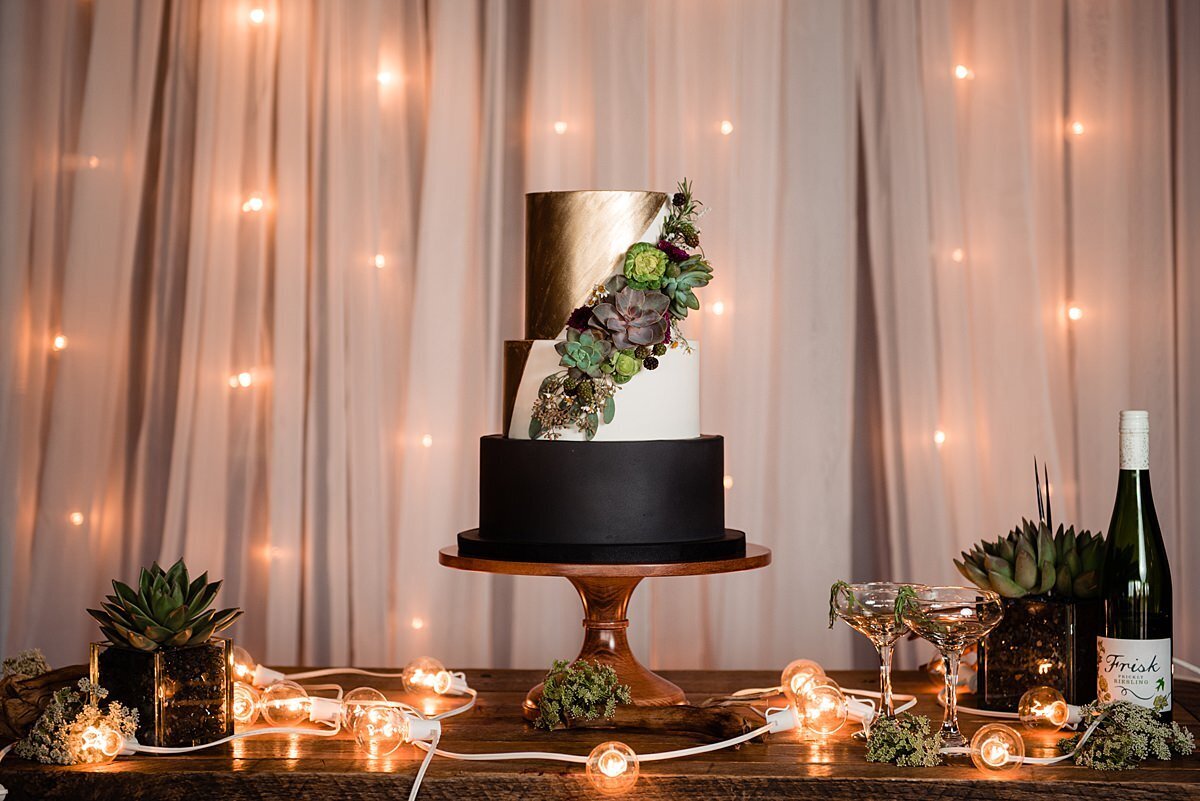 Moody black and gold wedding cake decorated with succulents and string lights at City Winery Nashville