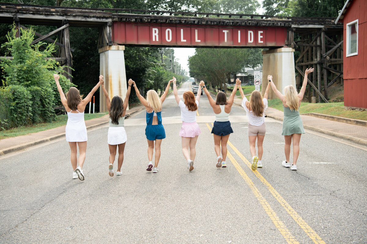 Women with their hands in the air walking under an Alabama bridge sign