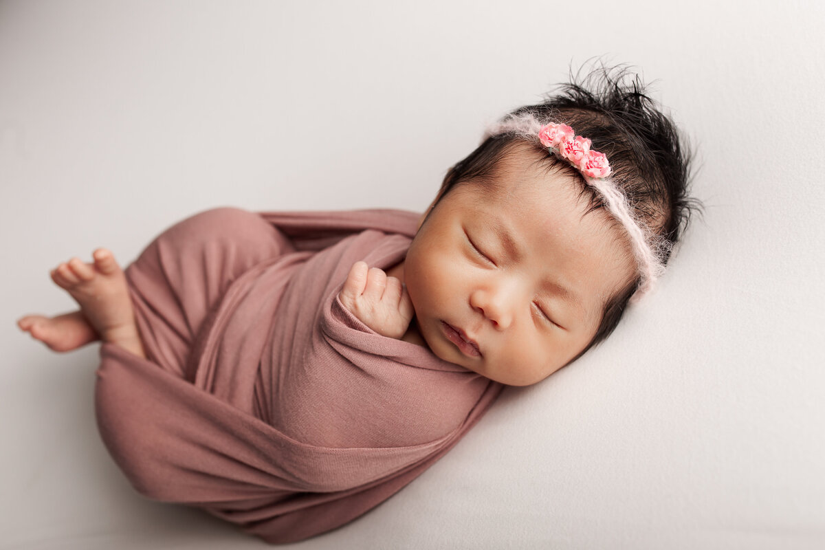 newborn girl wrapped in a pink wrap wearing a pink headband