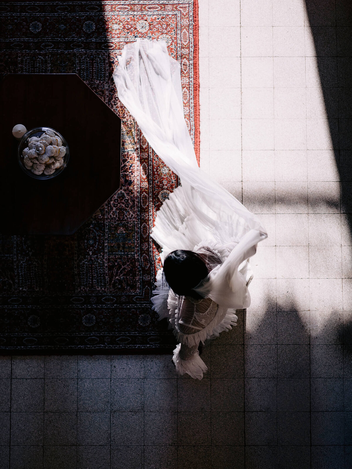 Top view of the bride standing on a red carpet; on the side is a small brown table with a plate of pastries in the middle
