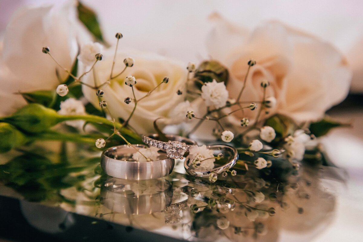 Two wedding rings nestled among white roses and baby's breath flowers, with a reflective surface beneath them, perfect for Iowa weddings.