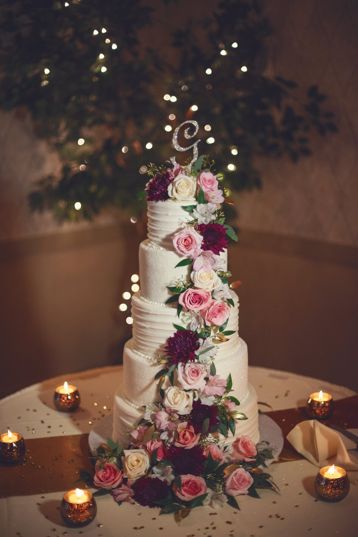 Wedding cake with pink and red roses by candles.