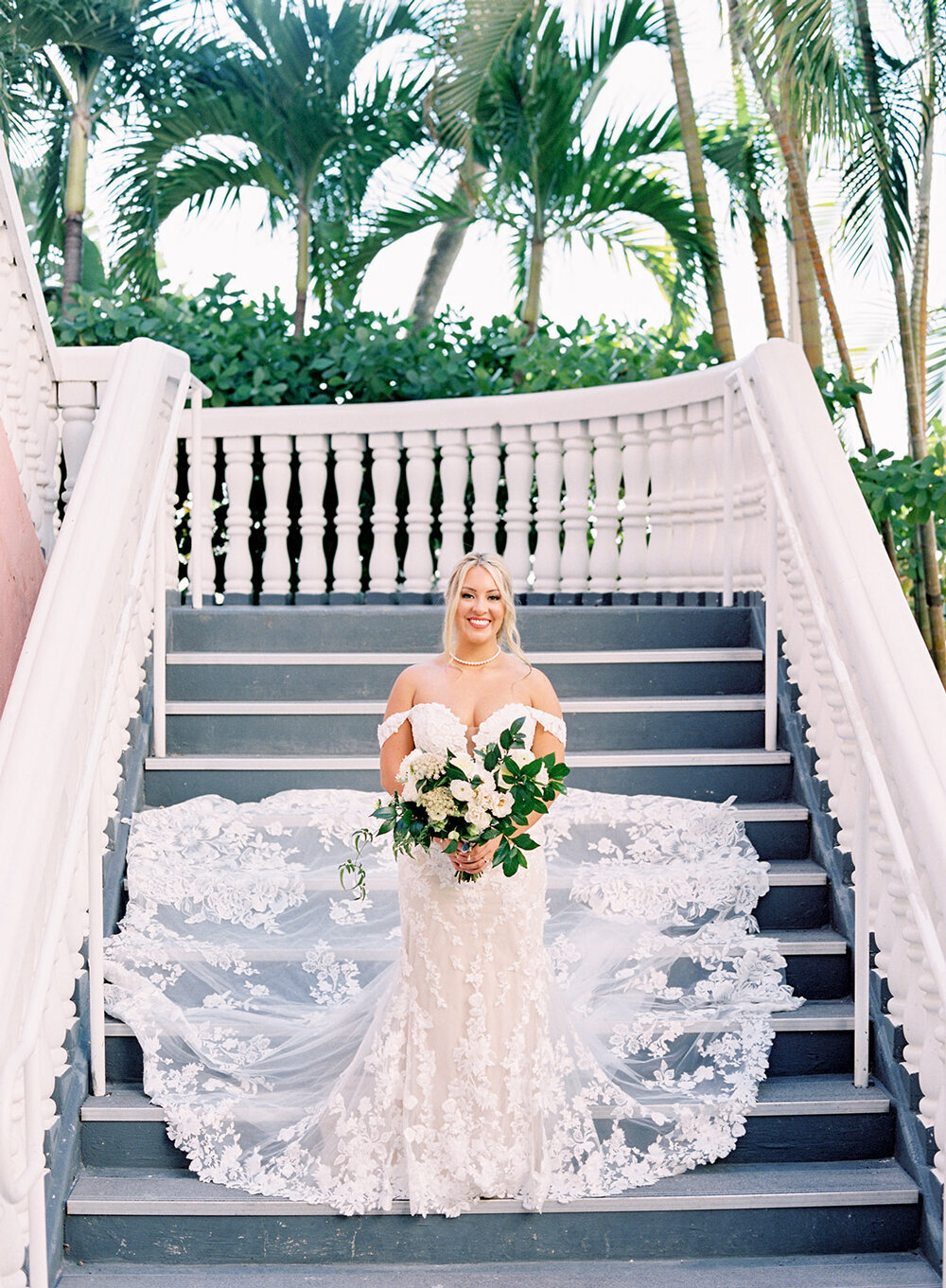 Stunning bride standing on the stairs at Don Cesar Hotel, St. Pete Beach, FL, with her lace train cascading beautifully down the steps during a December wedding.