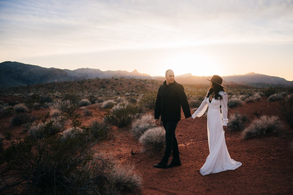 An enchanting elopement scene at Valley of Fire in Las Vegas, where the couple walks hand in hand against the backdrop of a stunning sunset, creating a moment filled with love and warmth.