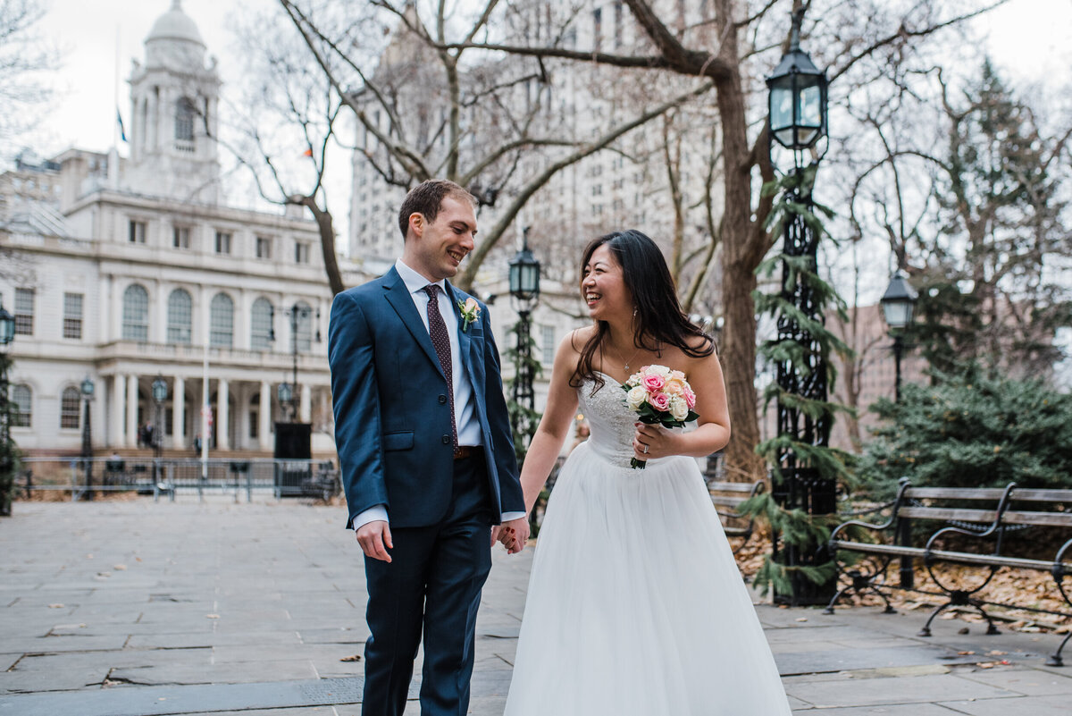 Bride and Groom in a white wedding gown and blue suit holding hands outside of City Hall in Philadelphia.
