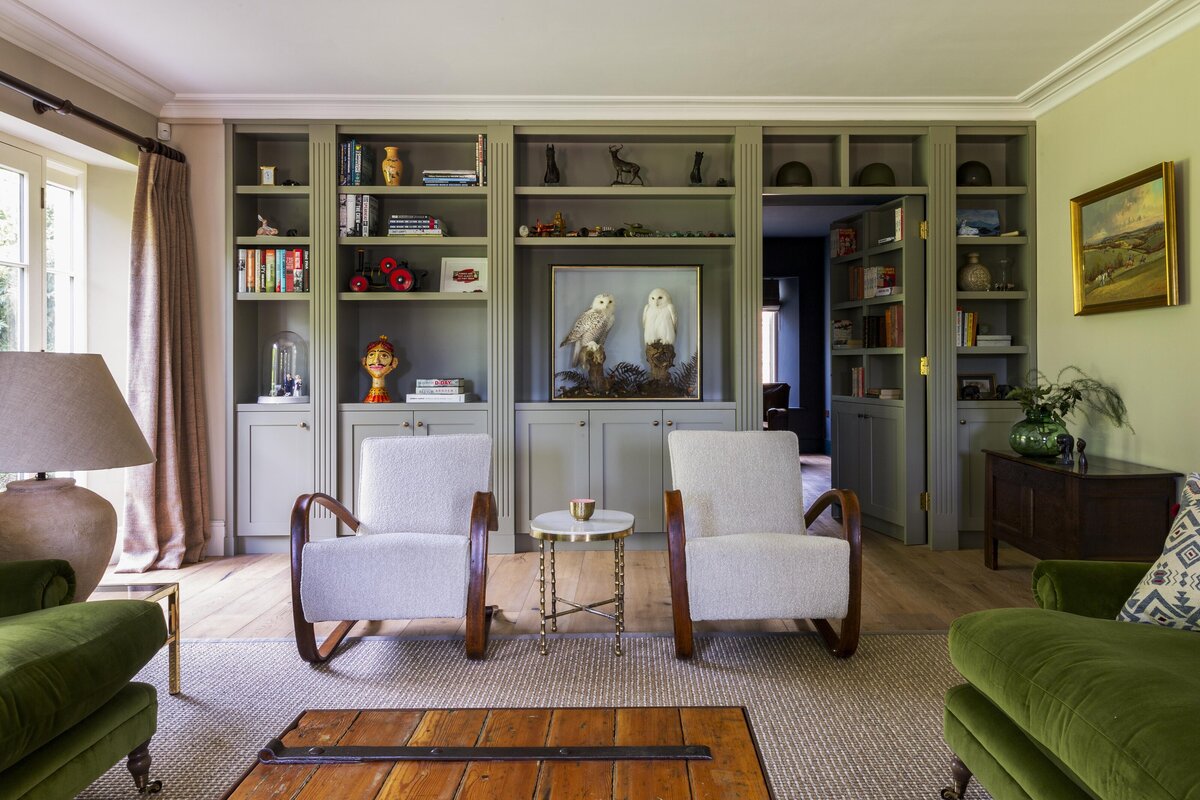 Living room and library with green cabinetry and two armchairs