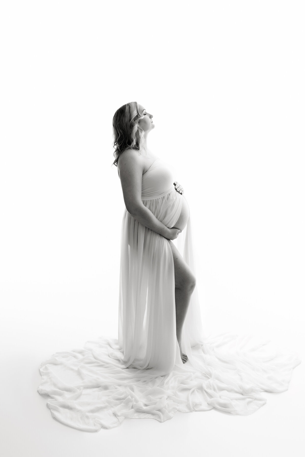 A mom to be holds her bump while proudly standing in a studio