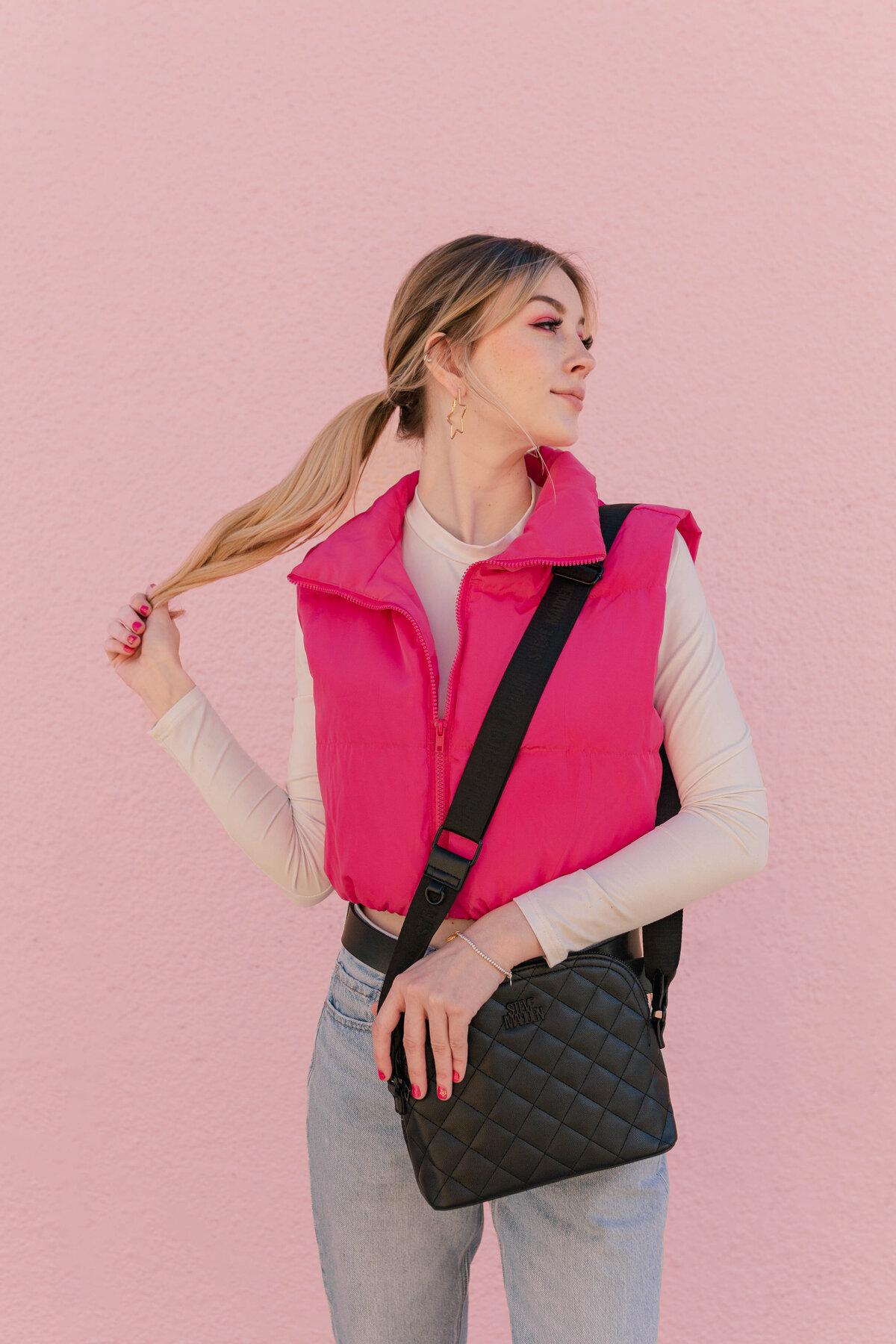 Sporty Barbie model poses in front of a pink wall with a hot pink vest and black purse on Westheimer