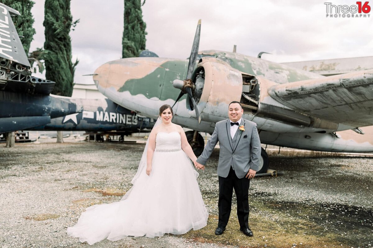 Newly married couple hold hands in front of a classic war plane