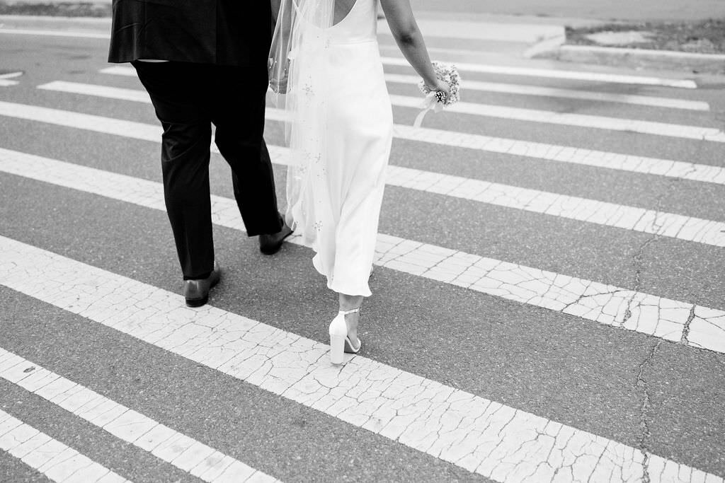 black and white photo of a bride and grooms legs as they walk across a city street