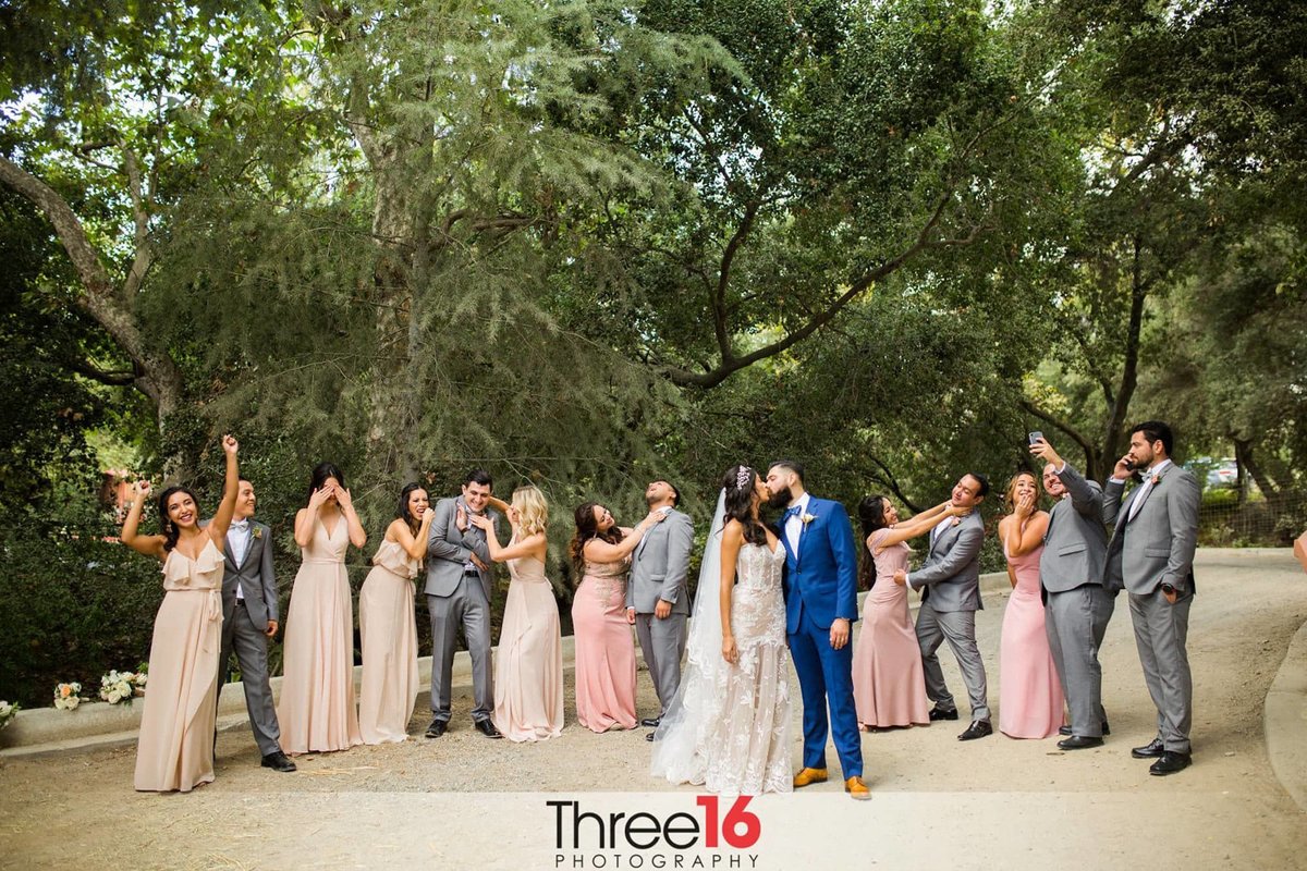 Bride and Groom share a kiss while Bridal Party act silly