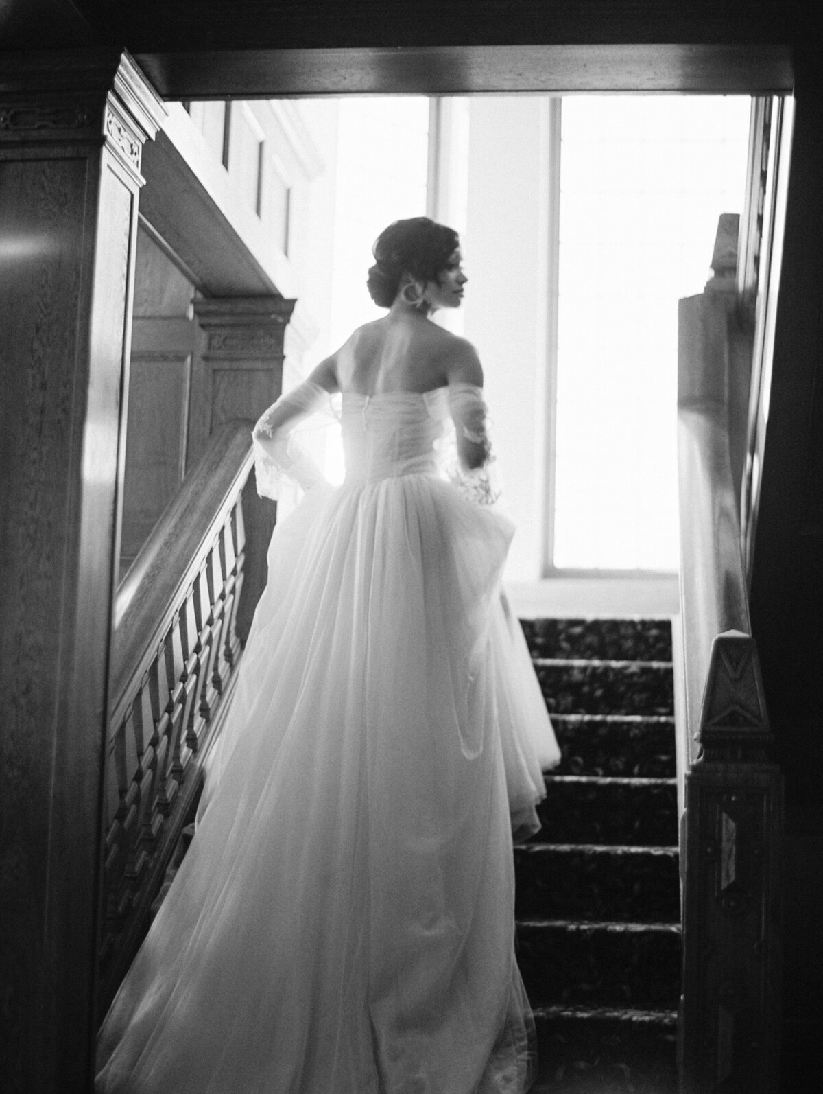 black and white photo of a bride walking on some steps holding her dress and looking off into the distance at the lairmon manor in bellingham washington